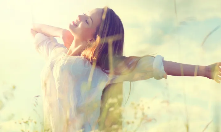 A smiling woman with arms outstretched enjoying the warm sunlight in a grassy field 