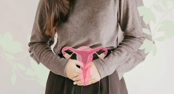A woman holding her lower abdomen with an illustration of the female reproductive system overlaid