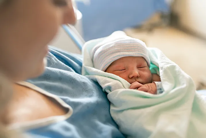 Mother holding her swaddled newborn baby in hospital