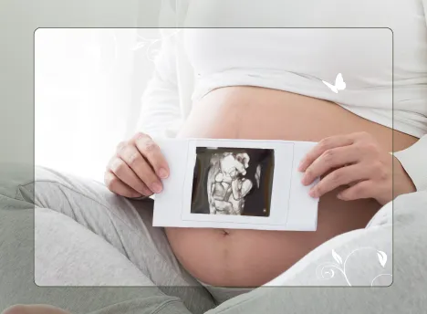 Pregnant woman holding a Foetal Anomaly Scan photo in front of her belly.